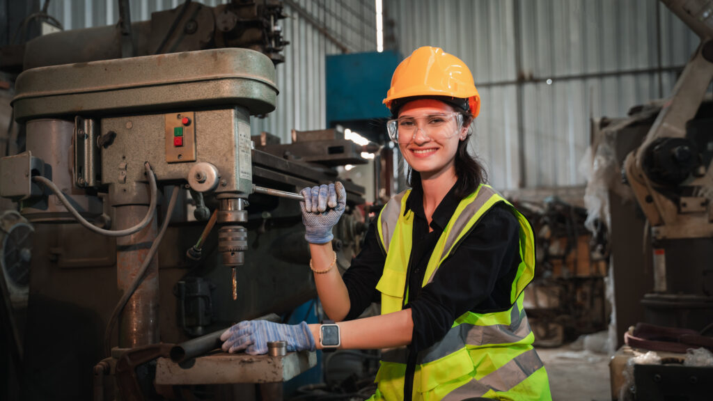 Female engineer operating industrial machinery in a factory, wearing safety gear — representing skilled trades eligible under the UK Skilled Worker visa.