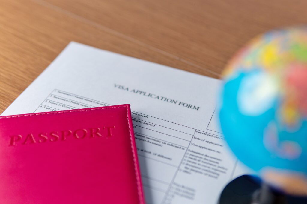 A red passport placed on top of a UK visa application form, with a small globe in the background.