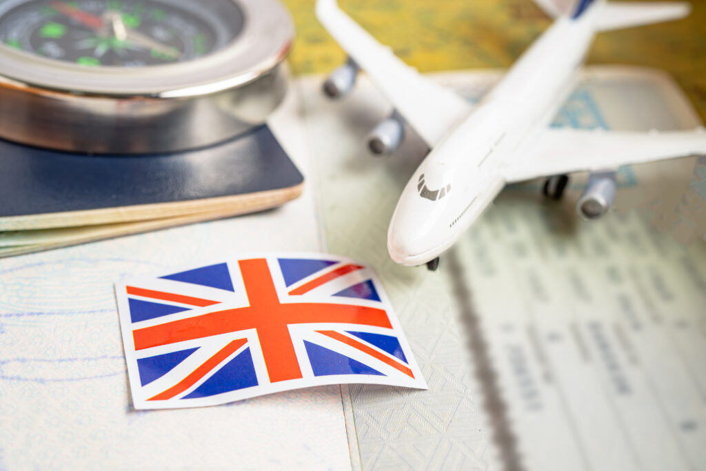 UK visa application with passport, compass, Union Jack flag, and airplane model — symbolising skilled worker visa sponsorship opportunities in 2025.