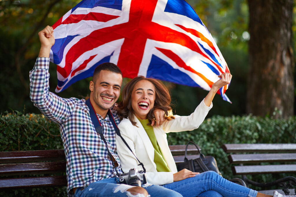 Happy young couple celebrating in the UK with Union Jack flag, symbolising opportunities under new Skilled Worker visa rules and RQF Level 6 requirements in 2025.