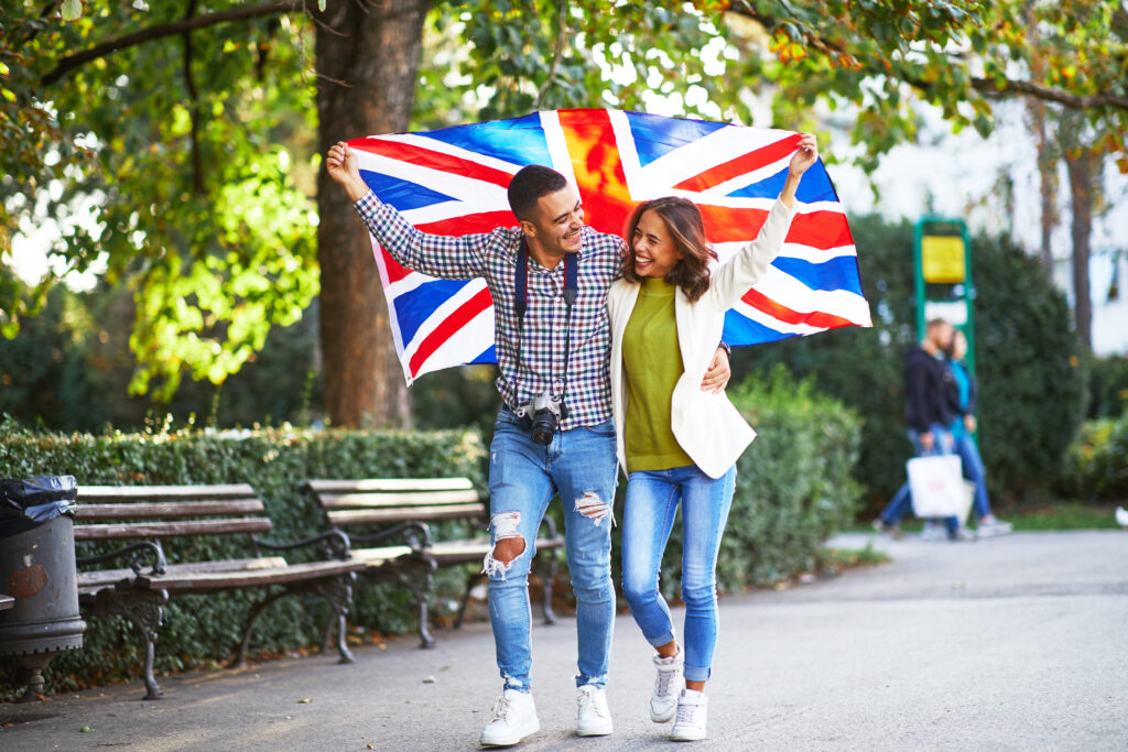Happy couple celebrating in the UK with a Union Jack flag, symbolising settlement after a Skilled Worker visa.
