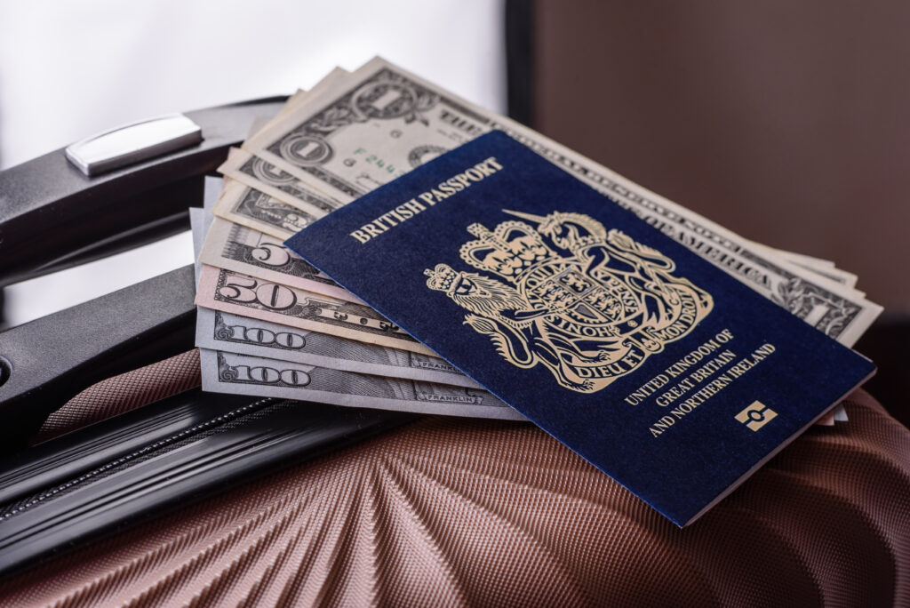 British passport placed on top of US dollar banknotes and a travel suitcase, symbolising global mobility and finance.