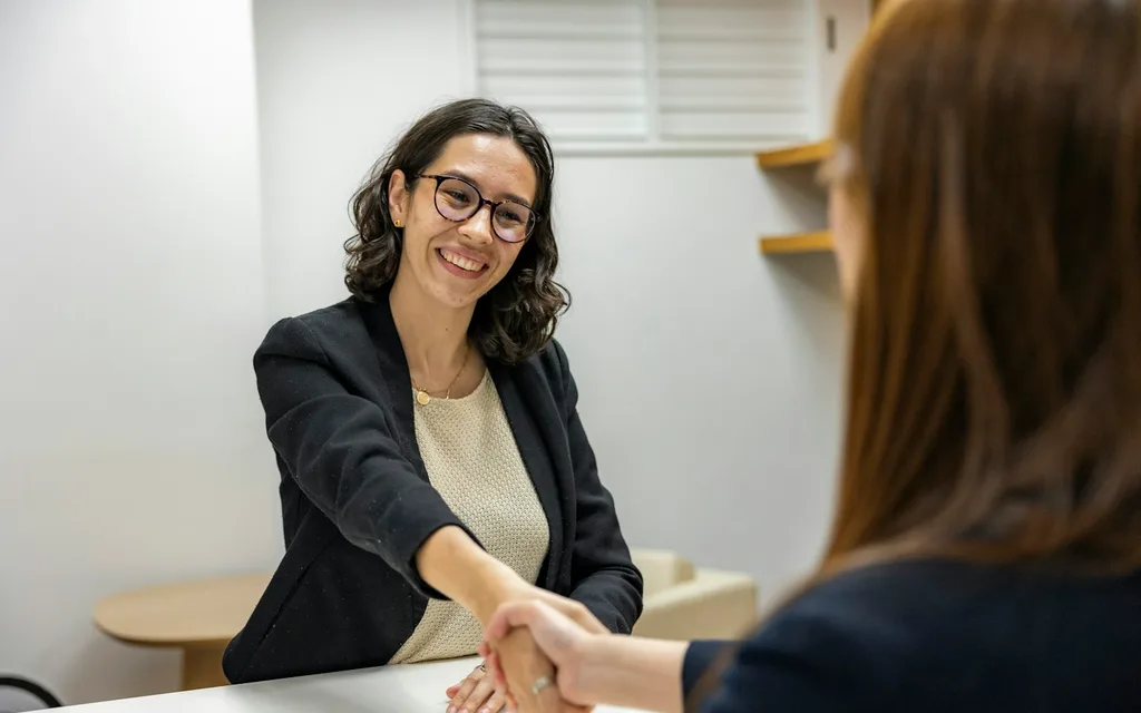 a woman shaking hands with another woman sitting at a table
